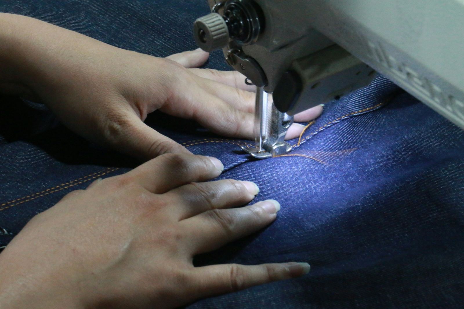 Hands guiding denim through an industrial sewing machine