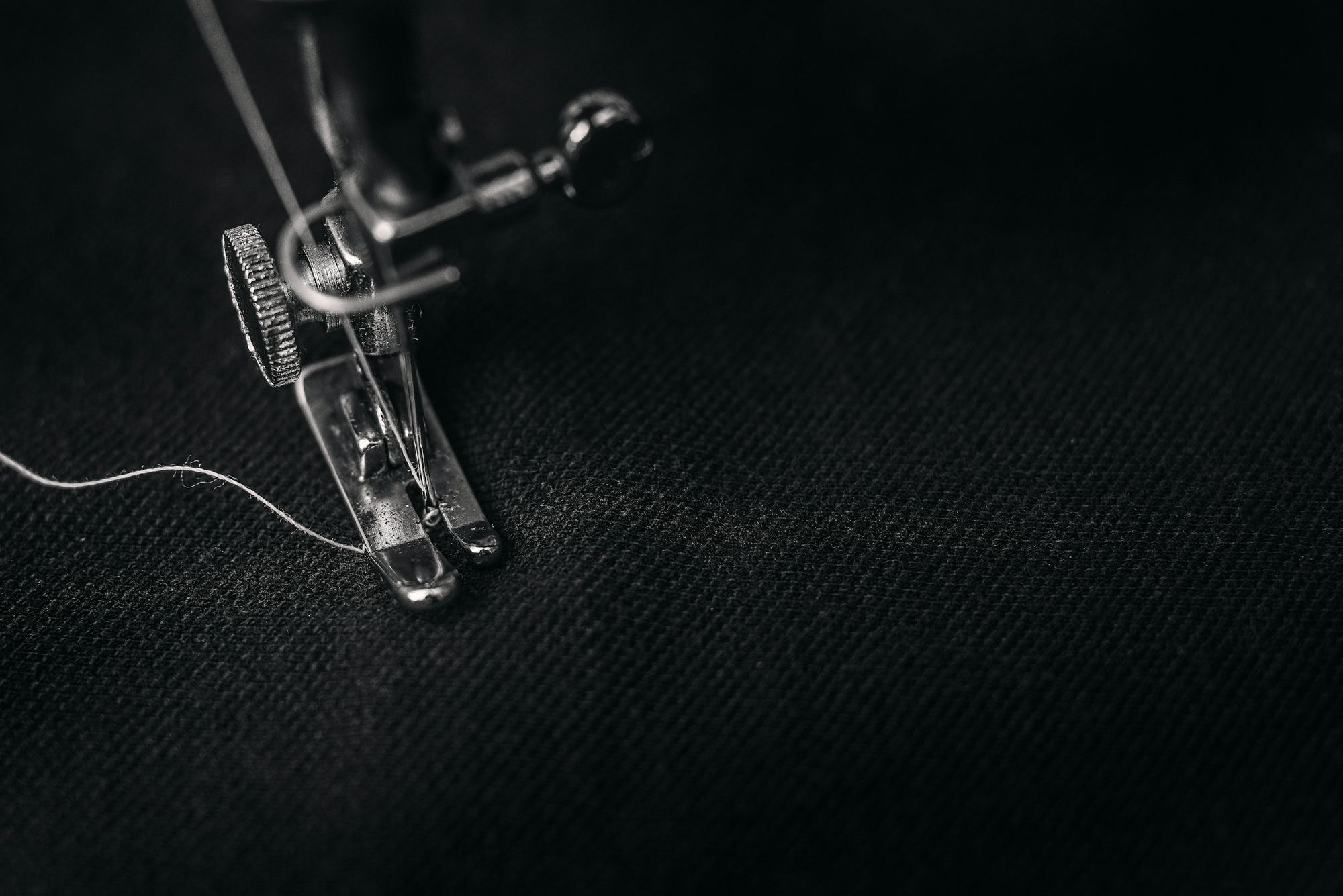 Close-up of a sewing machine presser foot and thread on dark fabric